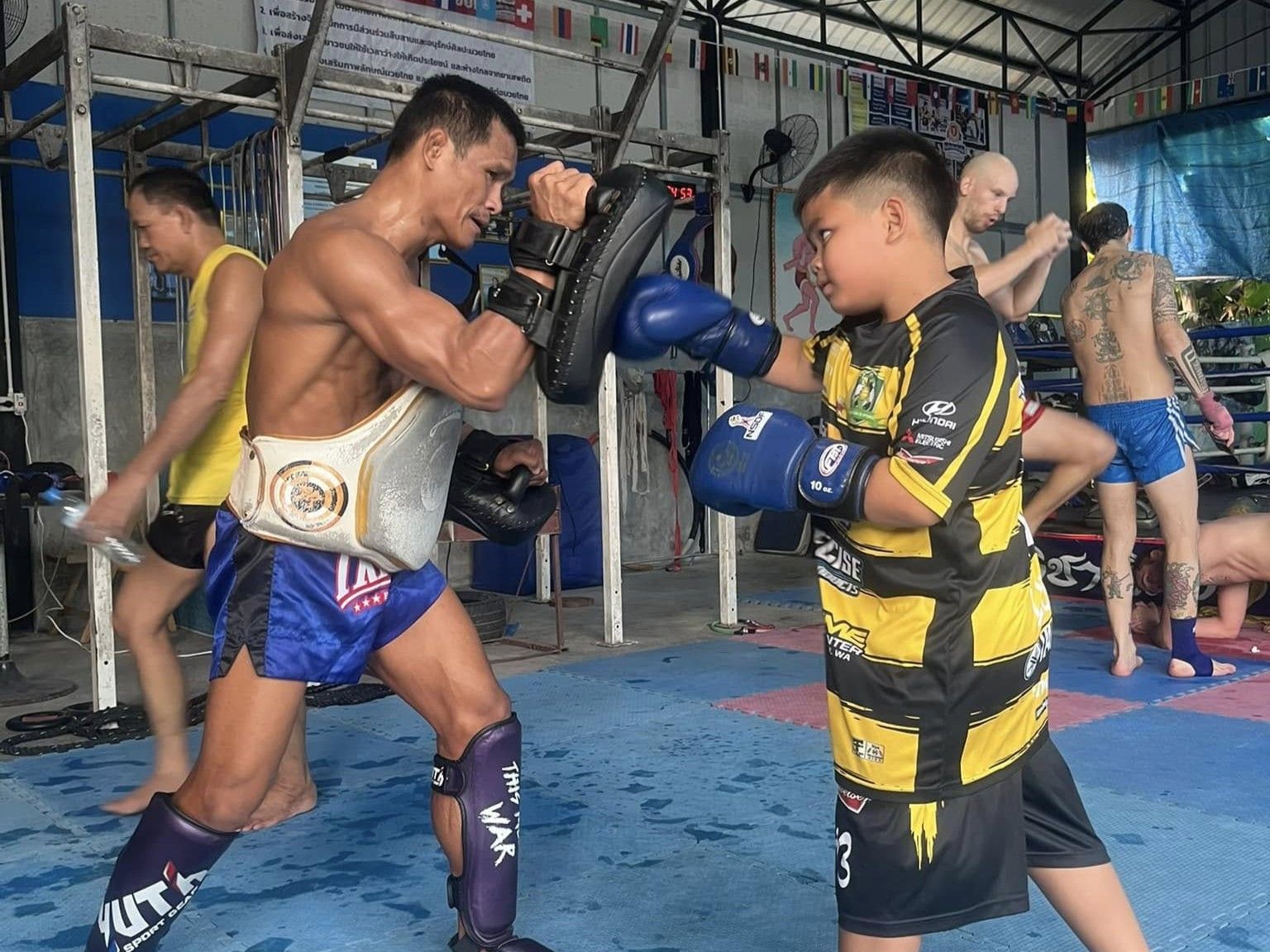 A trainer holding pads for a young student during Muay Thai training at J. Aphichat Muay Thai Gym, Sing Buri
