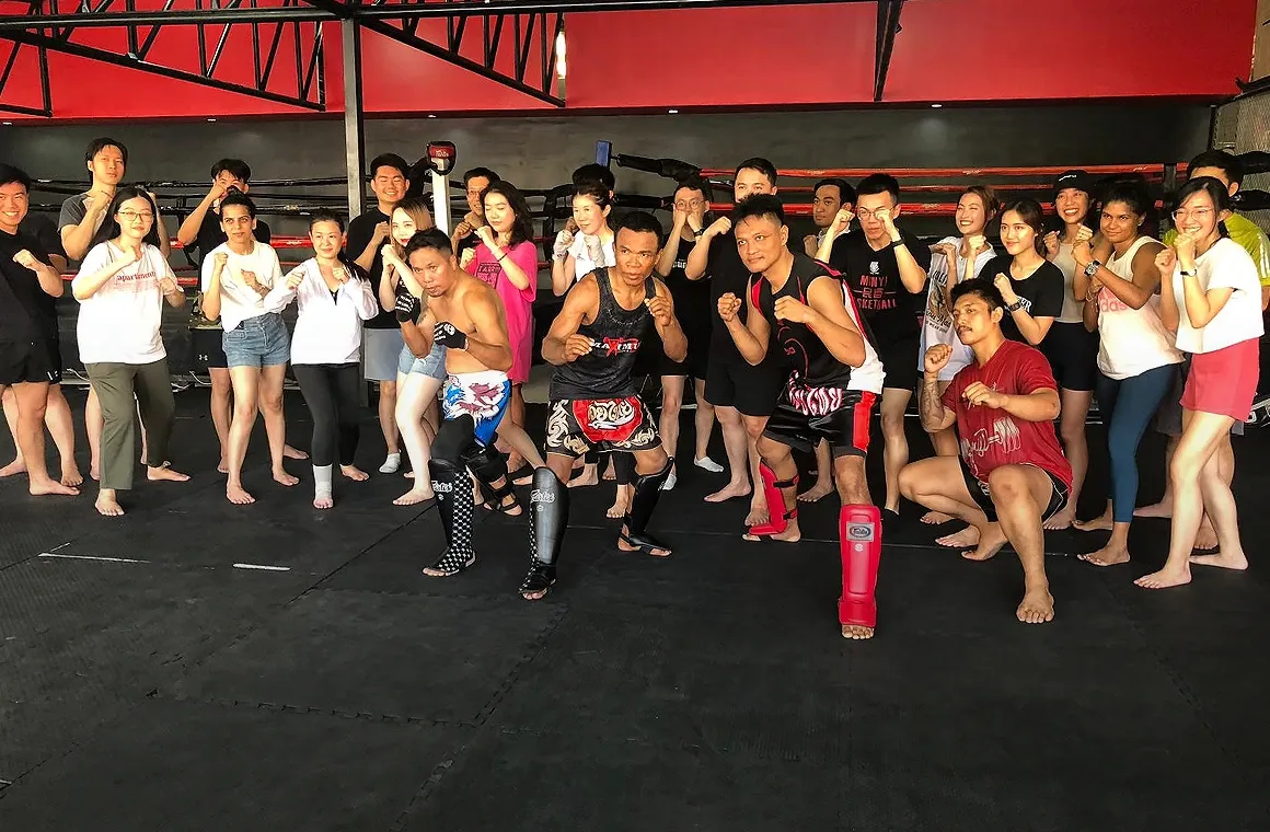 Trainers and students posing together with fighting stances before a Muay Thai class begins at Maximum Muay Thai & Fitness Training Center, capturing a fun and energetic atmosphere that’s perfect for travelers looking to experience authentic Muay Thai training