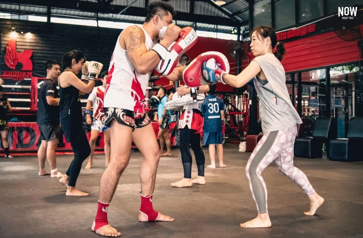 A woman practicing muay thai punches with a trainer at Kru Dam Gym in Bangkok