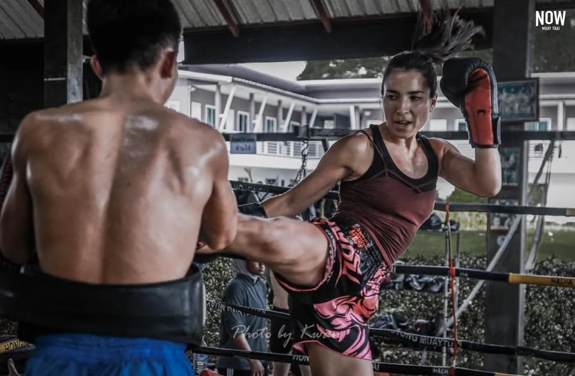 A woman practicing muay thai kicks at Hongthong Gym with a trainer