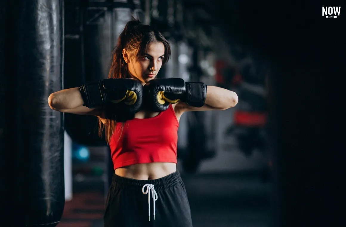 A high-angle shot captures a powerful female kickboxer posing with gloves, and looking serious