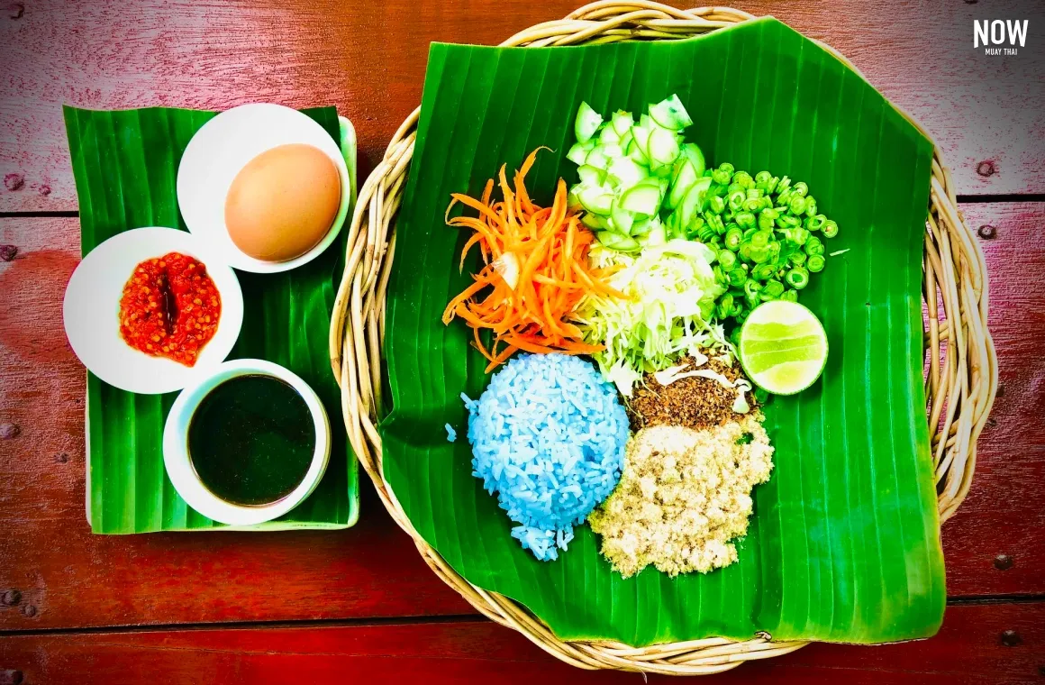 Top view of Thai blue rice with shredded vegetables, lime, chili paste, salted egg, and dipping sauce served on a banana leaf.