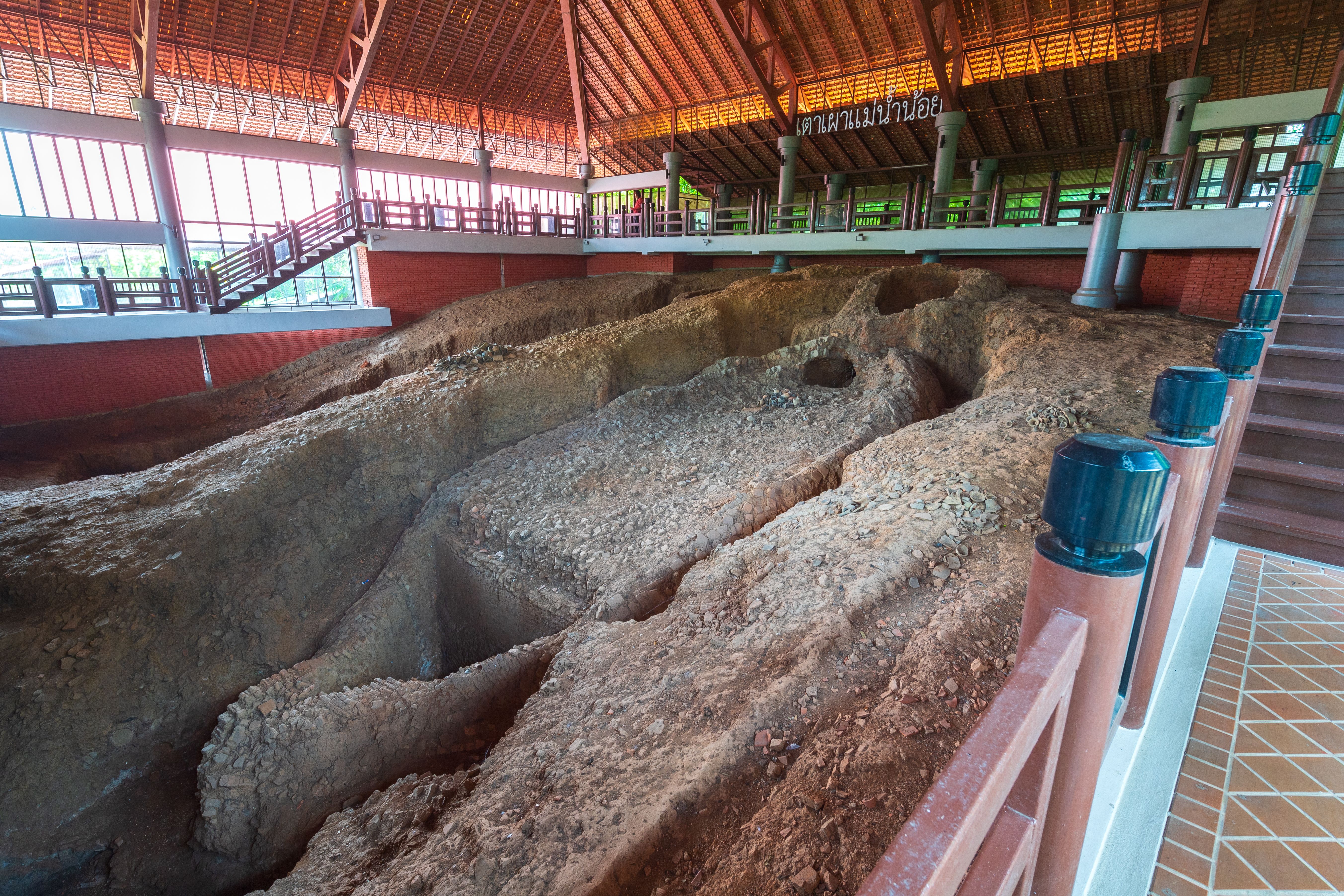 An ancient pottery kiln on display behind a barrier at the Mae Nam Noi Kiln Museum, Sing Buri
