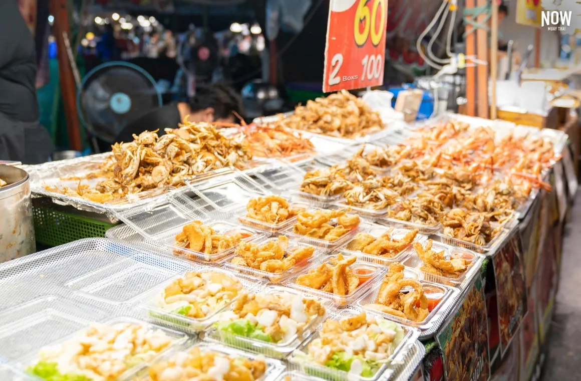 A colorful, close-up display of various fried seafood appetizers, including small whole crabs, fried crab roe, and fried shrimp, arranged on a tray ready for sale at a busy market stall.