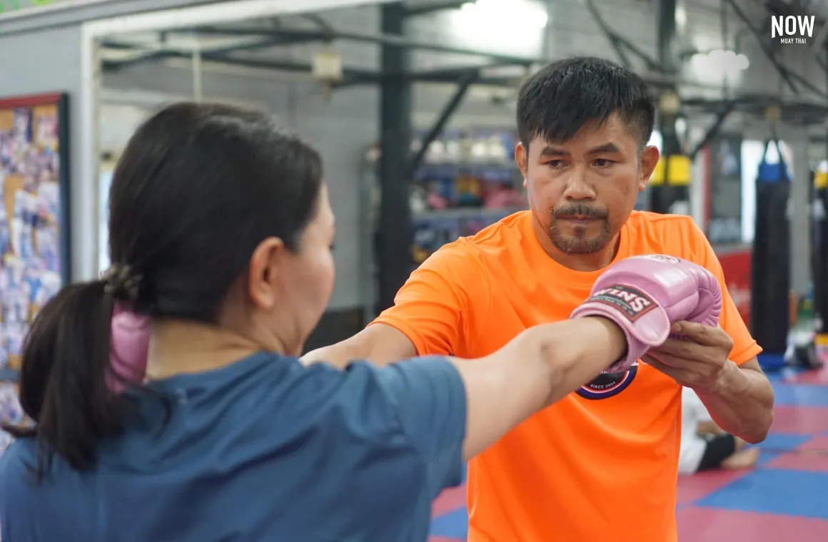 a woman practicing muay thai punches with a trainer at Jaroenthong Muay Thai Gym Bangkok