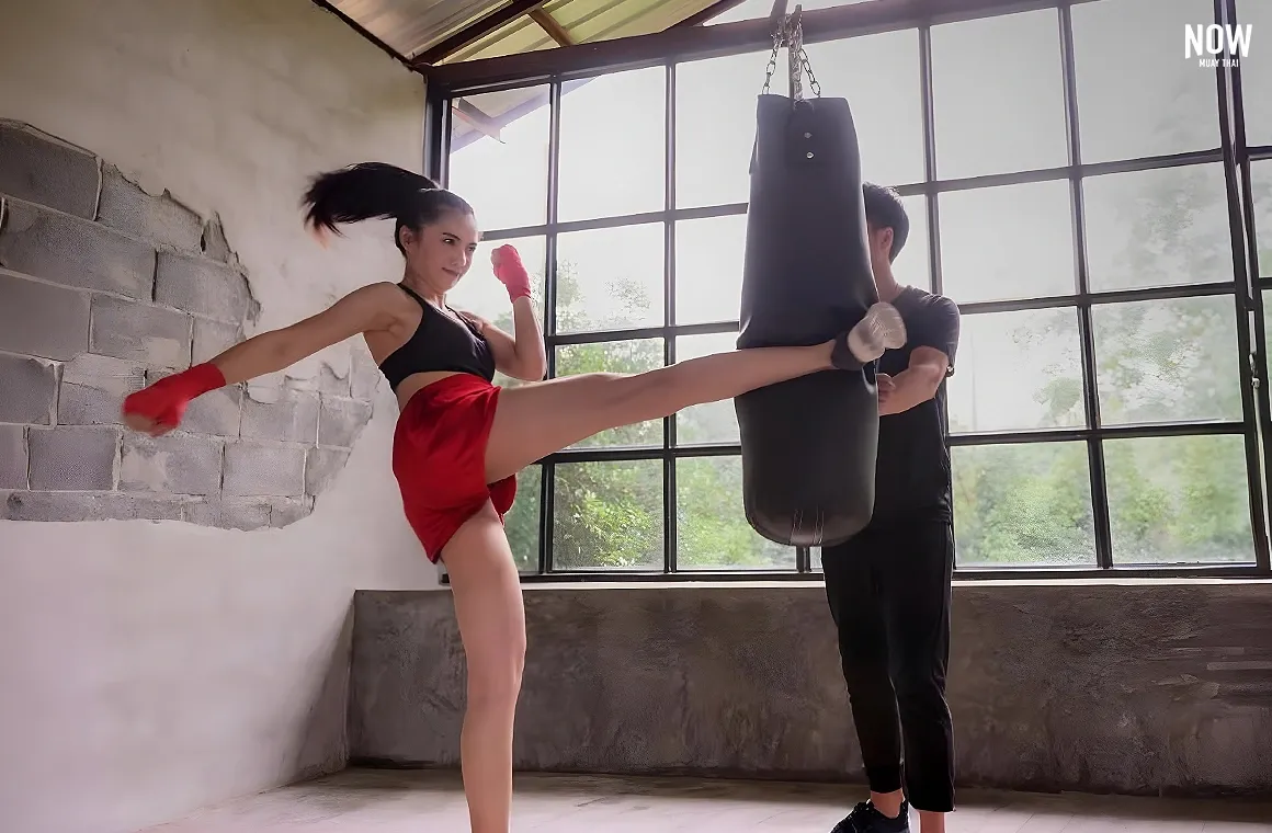 A woman delivering a powerful kick to a heavy bag in a Muay Thai training session, showcasing the intense, fat-burning potential of this full-body workout. Her focused energy and controlled movement highlight why Muay Thai is celebrated as the ultimate calorie-burning and muscle-toning exercise.