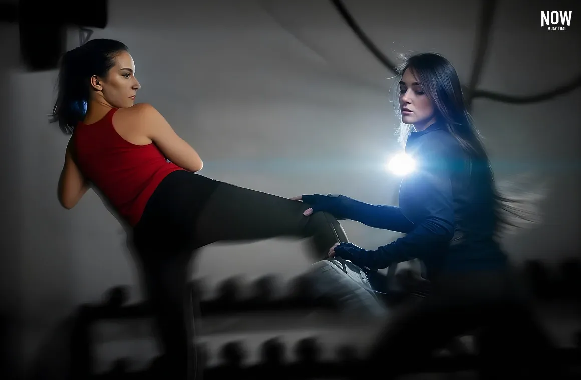 Two women engage in an intense Muay Thai demonstration, with one showcasing defensive skills against the other's powerful kick. This action-packed moment highlights how Muay Thai builds not only physical strength but also focus, discipline, and practical self-defense skills. The confidence and inner strength they exude show how this training fosters resilience and mental well-being, making it an empowering workout for women.