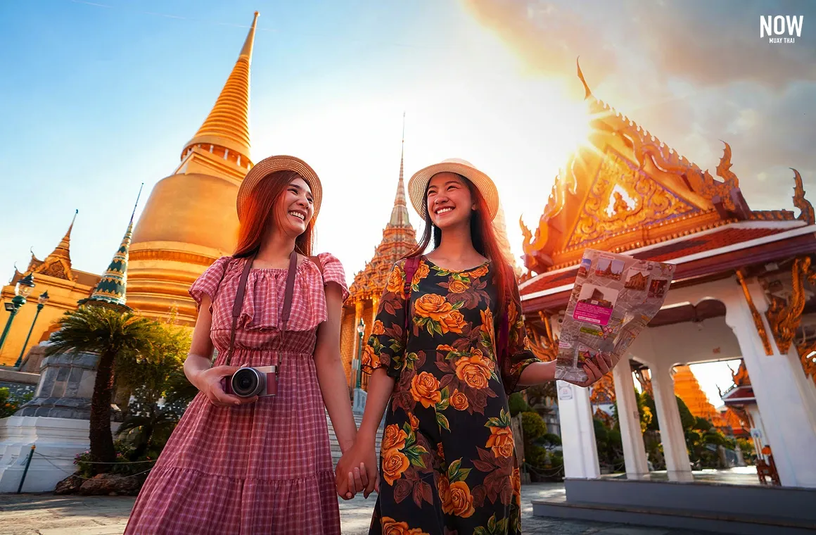 Two female tourists admiring the beauty of Wat Phra Kaew under the golden sunlight, reflecting off the temple's ornate roof.
