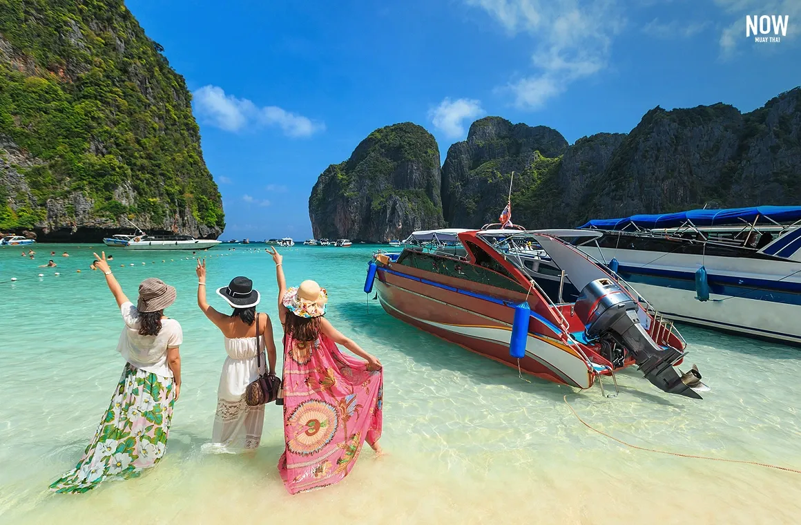 A group of female tourists waving and enjoying the breathtaking scenery of Maya Bay, one of Thailand's world-renowned destinations.
