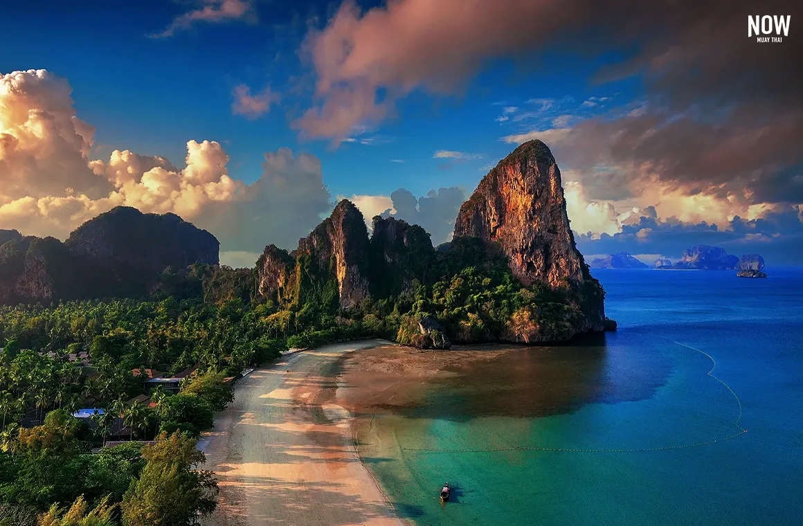 A breathtaking view of Railay Beach in Krabi, with crystal-clear turquoise waters, towering limestone cliffs, and soft white sand.
