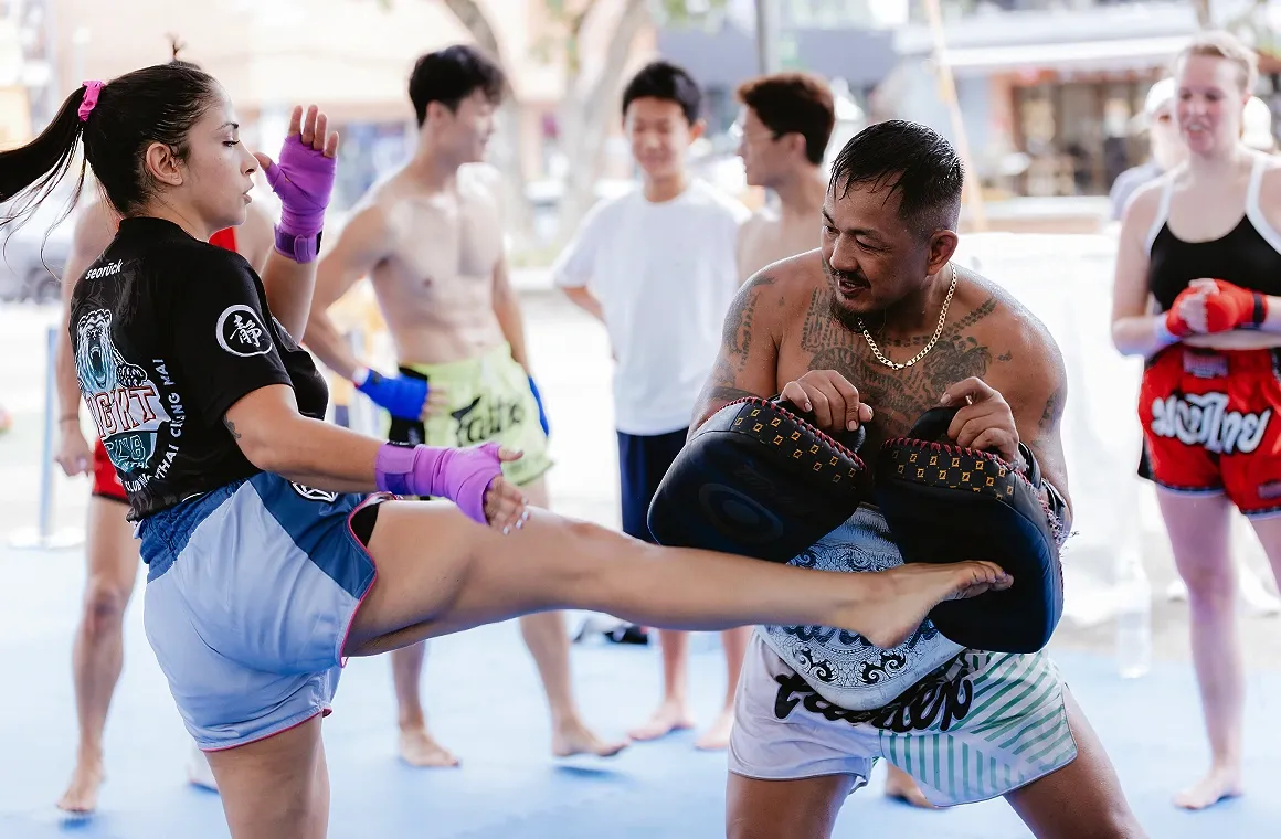 Trainer Gae (Suthat Muangmun), renowned head trainer at Elite Boxing Thailand and a popular figure in the Muay Thai circuit, holding pads for a student practicing kicks during a Muay Thai training session. Known for his worldwide Muay Thai seminars, Trainer Gae showcases expert technique and guidance.