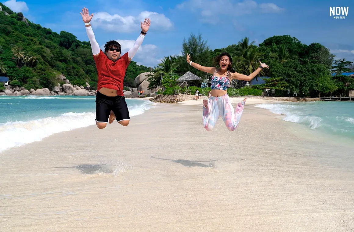 Joyful man and woman jumping above the sandy beach and turquoise waves of Koh Nangyuan Island, a stunning travel and Muay Thai training destination in Surat Thani, Thailand.