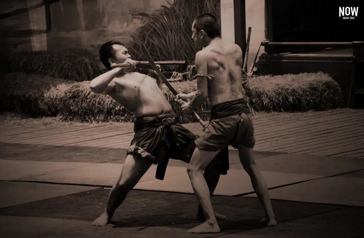 Two warriors engaged in a fierce battle, showcasing traditional Muay Boran techniques while wielding swords. Their fluid movements combine martial arts skills and weapon combat, representing the ancient fighting style of Thailand's warriors.