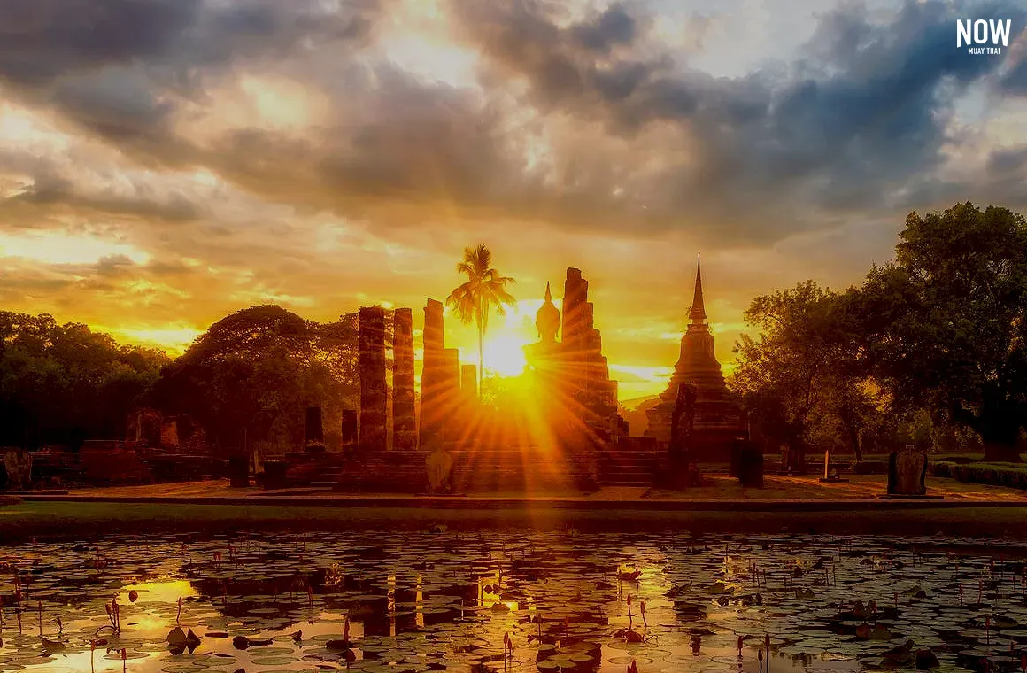 A majestic Big Buddha statue illuminated by the soft glow of sunrise at a temple in Ayutthaya, symbolizing the golden era of Muay Boran. The serene scene reflects the historical significance of Ayutthaya as the birthplace of Muay Boran, blending Thailand's spiritual and martial heritage.