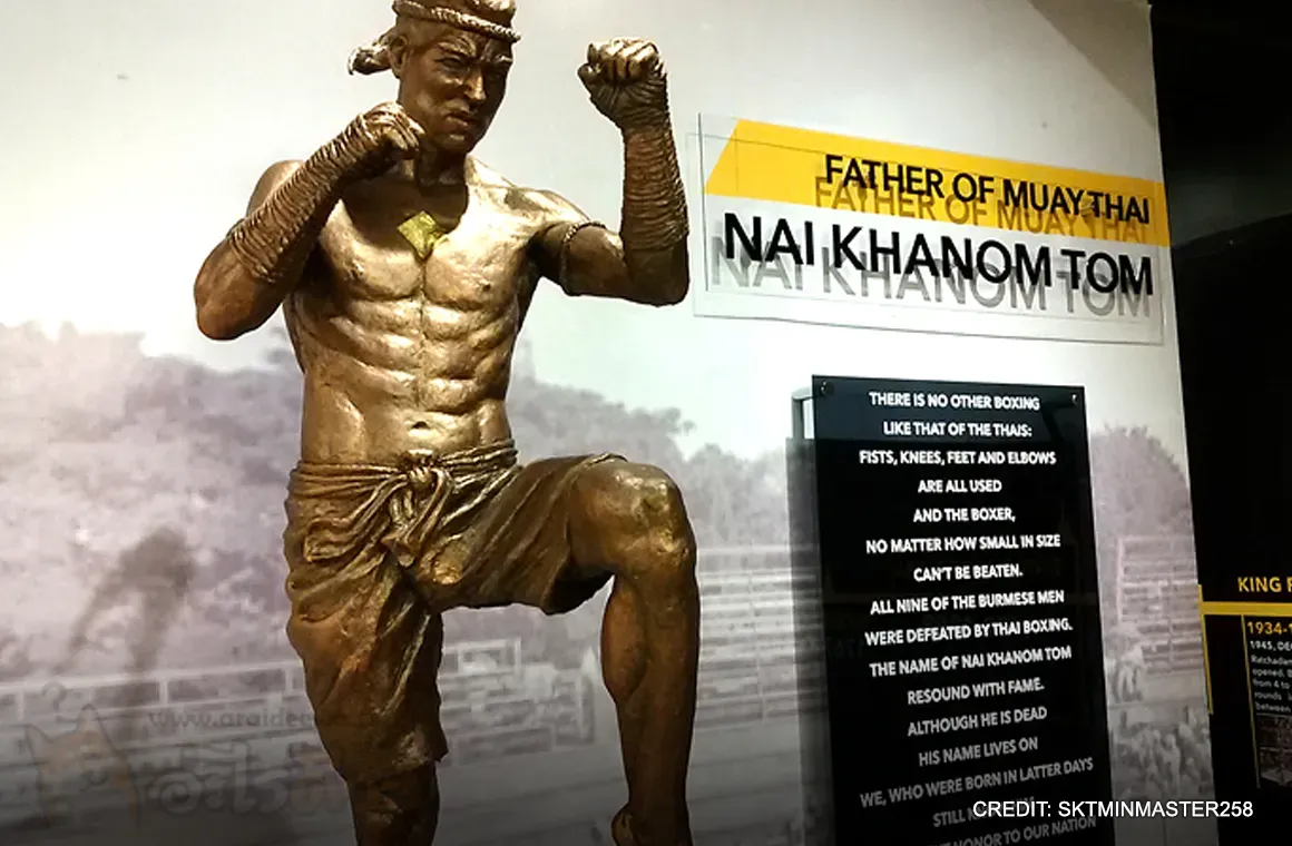 A statue of Nai Khanom Tom, the legendary Muay Thai fighter, revered as the "Father of Muay Thai." The image captures him in a traditional fighting stance, symbolizing his historic victory over Burmese fighters and his enduring legacy in Thai martial arts.