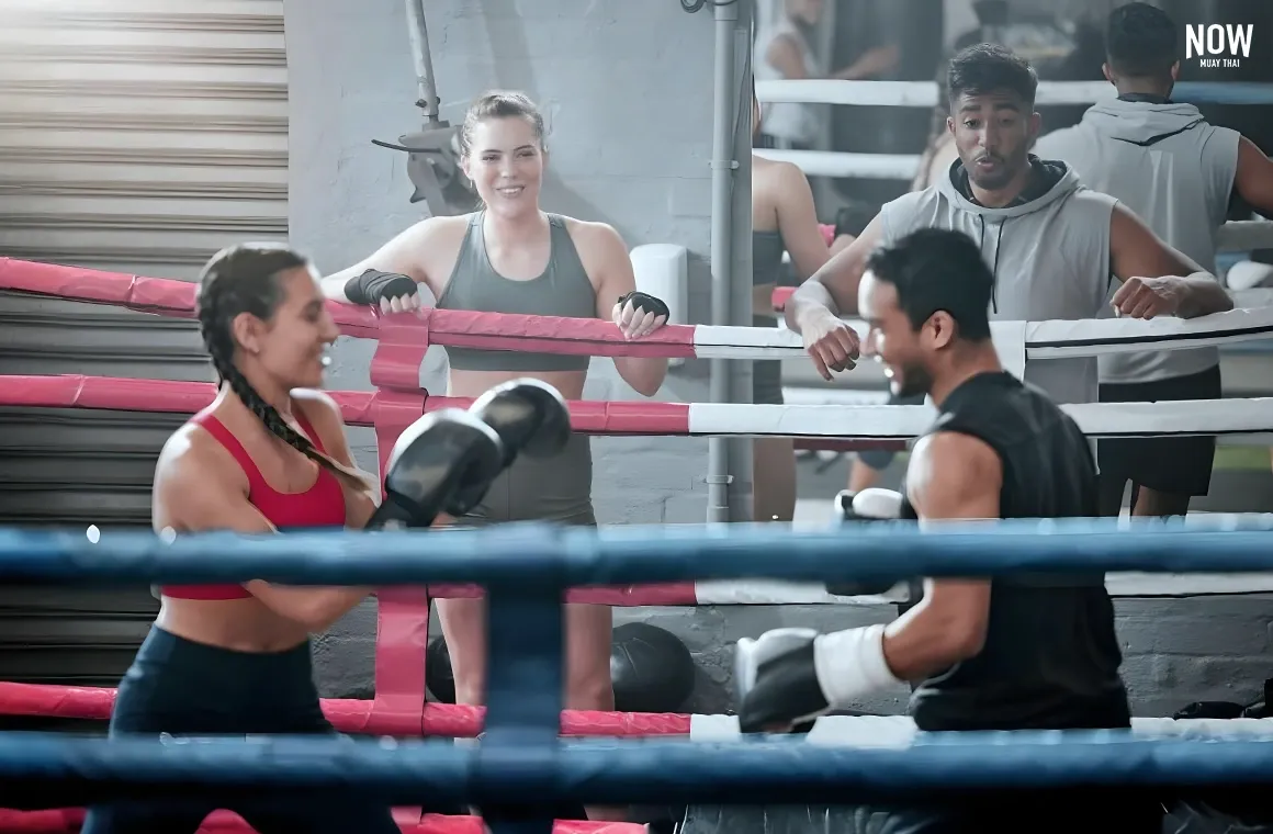 A female student enjoying her Muay Thai training in the boxing ring with her instructor. The class is filled with positive energy as the teacher guides her through each move, offering support and ensuring she progresses at her own pace. The instructor provides motivation and technique corrections, creating a fun and engaging learning environment.