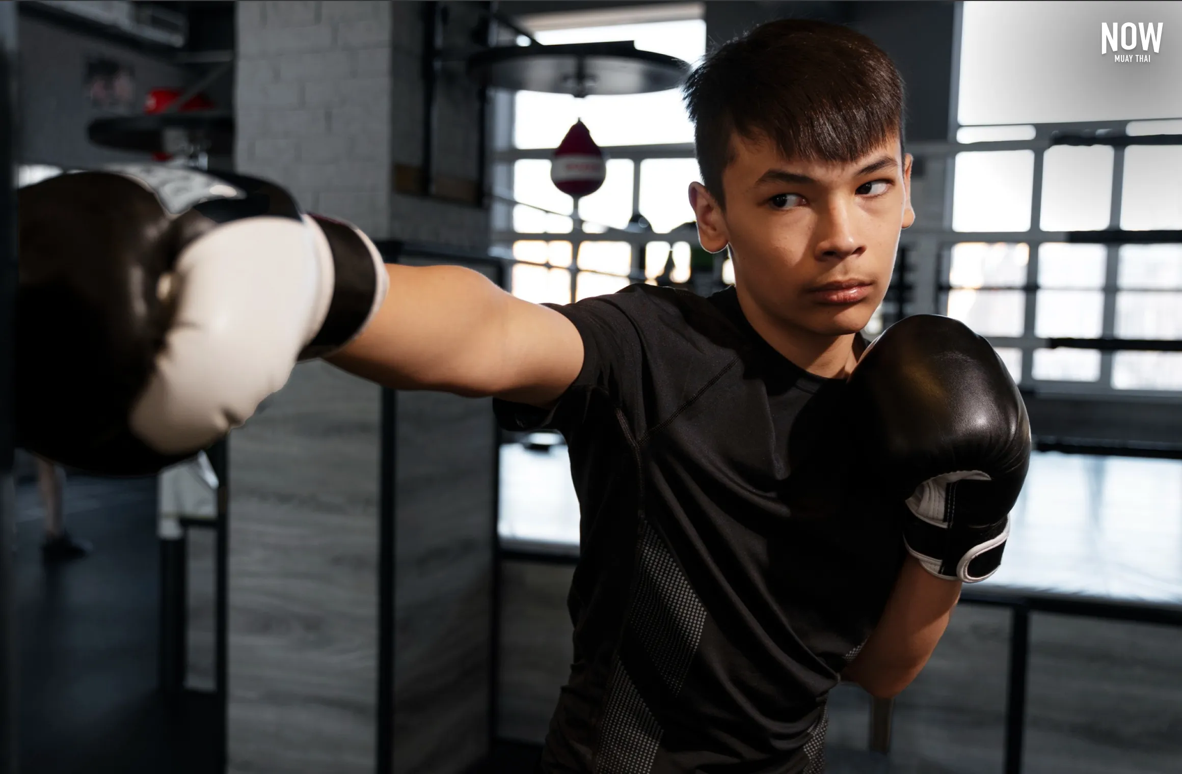 Boy training Muay Thai with bag gloves, hitting a heavy bag for impact resistance.
