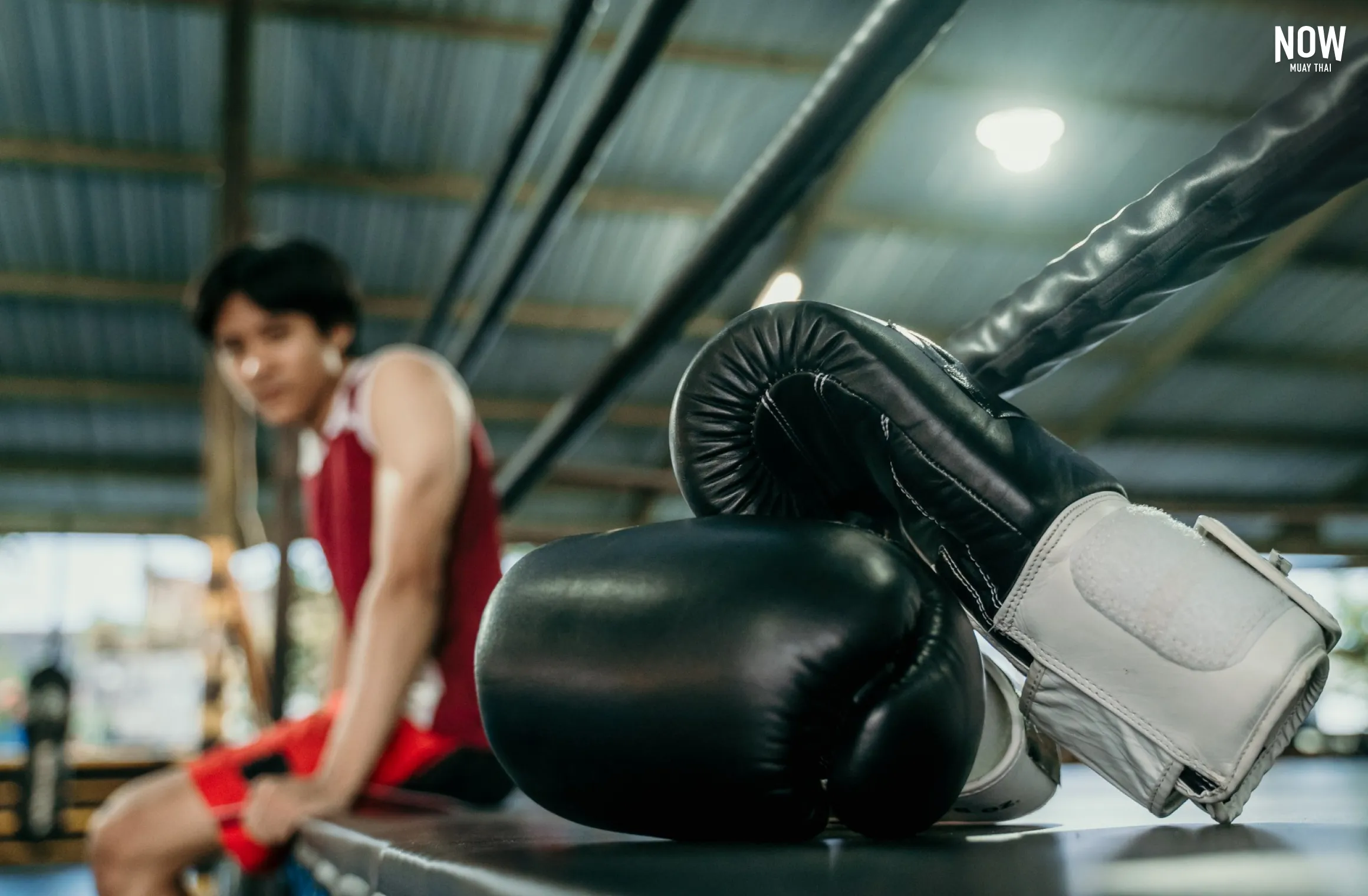 Muay Thai fighter resting next to his training gloves in the gym, highlighting the connection between fighter and essential gear.