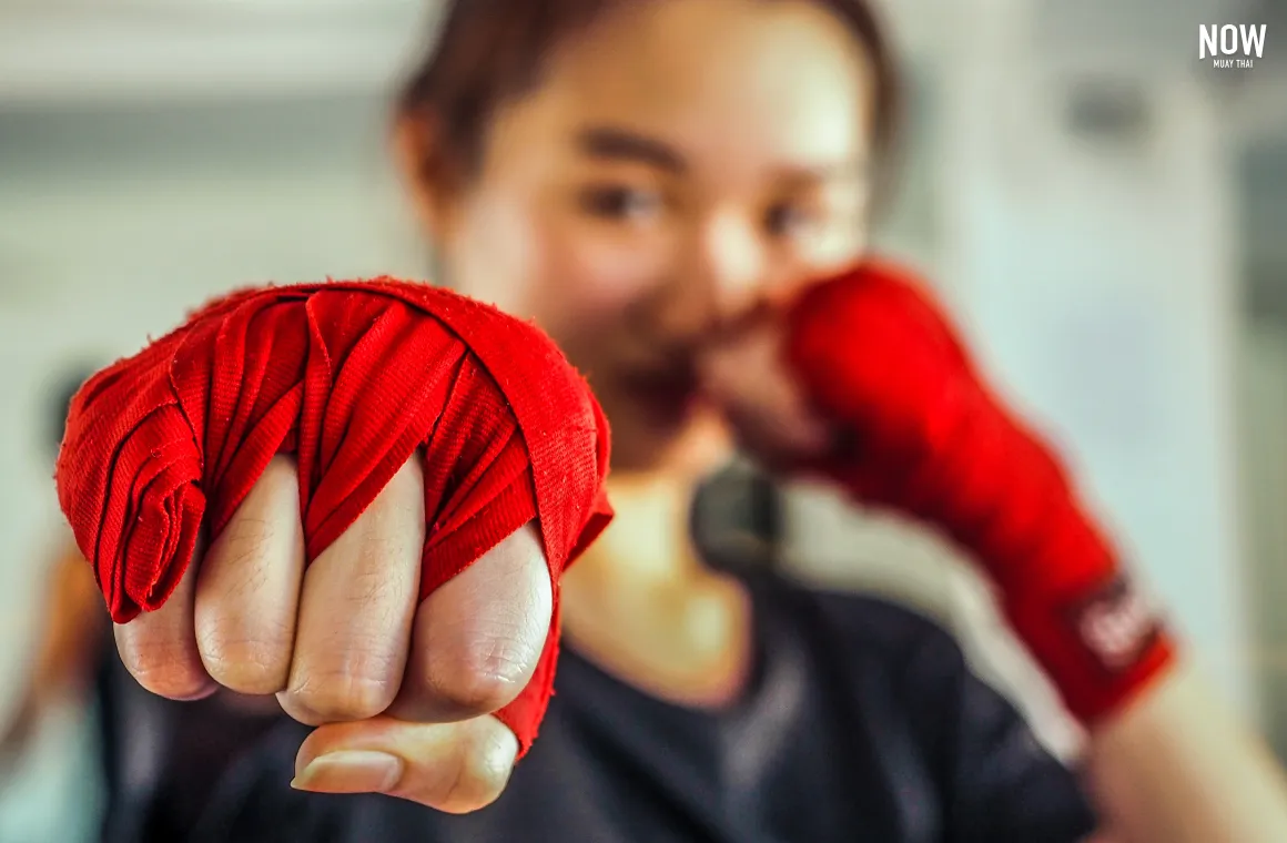 A woman wraps her hands in preparation for Muay Thai training, demonstrating the proper way to protect the fists before punching. Hand wrapping is an essential step every Muay Thai beginner should know before starting any workout or technique practice.