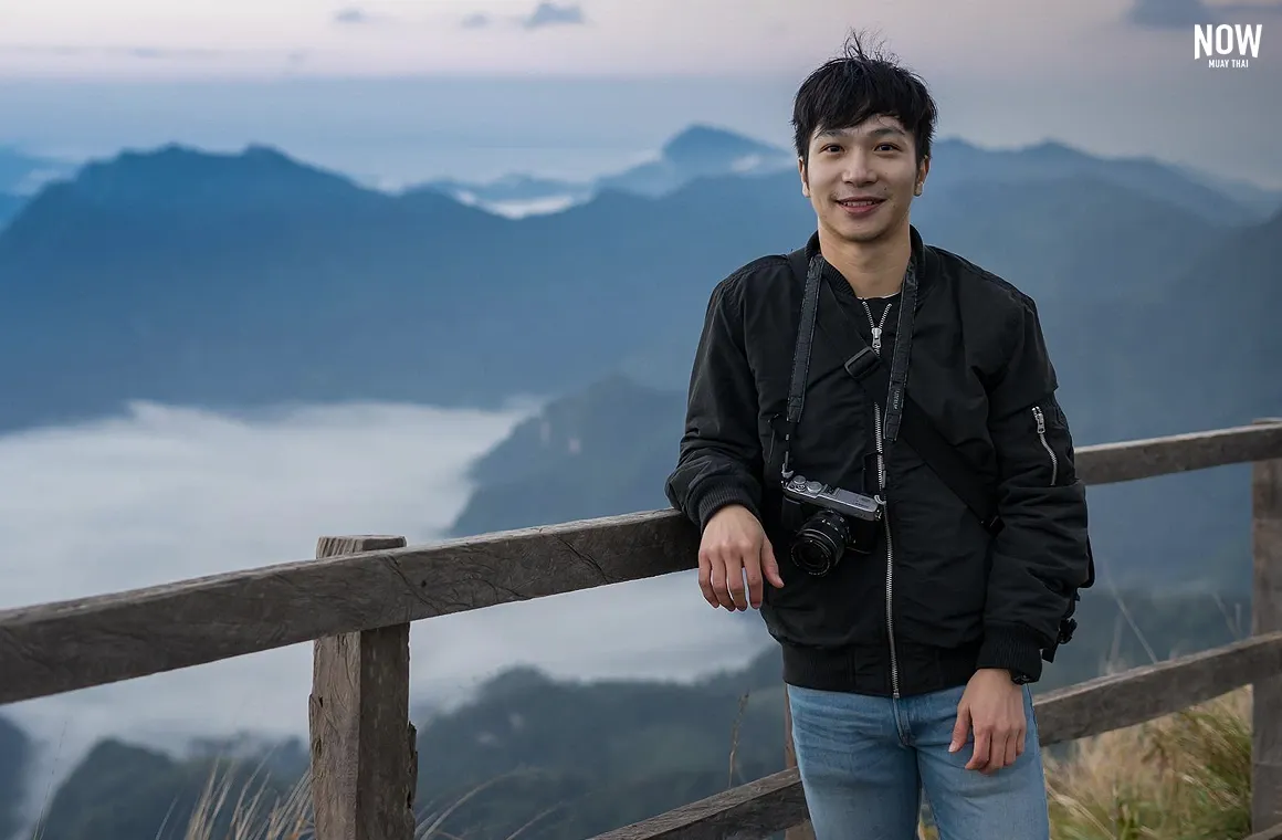 A smiling man stands atop Doi Ang Khang, Chiang Mai, with stunning mountain peaks and a golden sunset behind him, capturing the serenity and breathtaking beauty of this iconic Thai destination.
