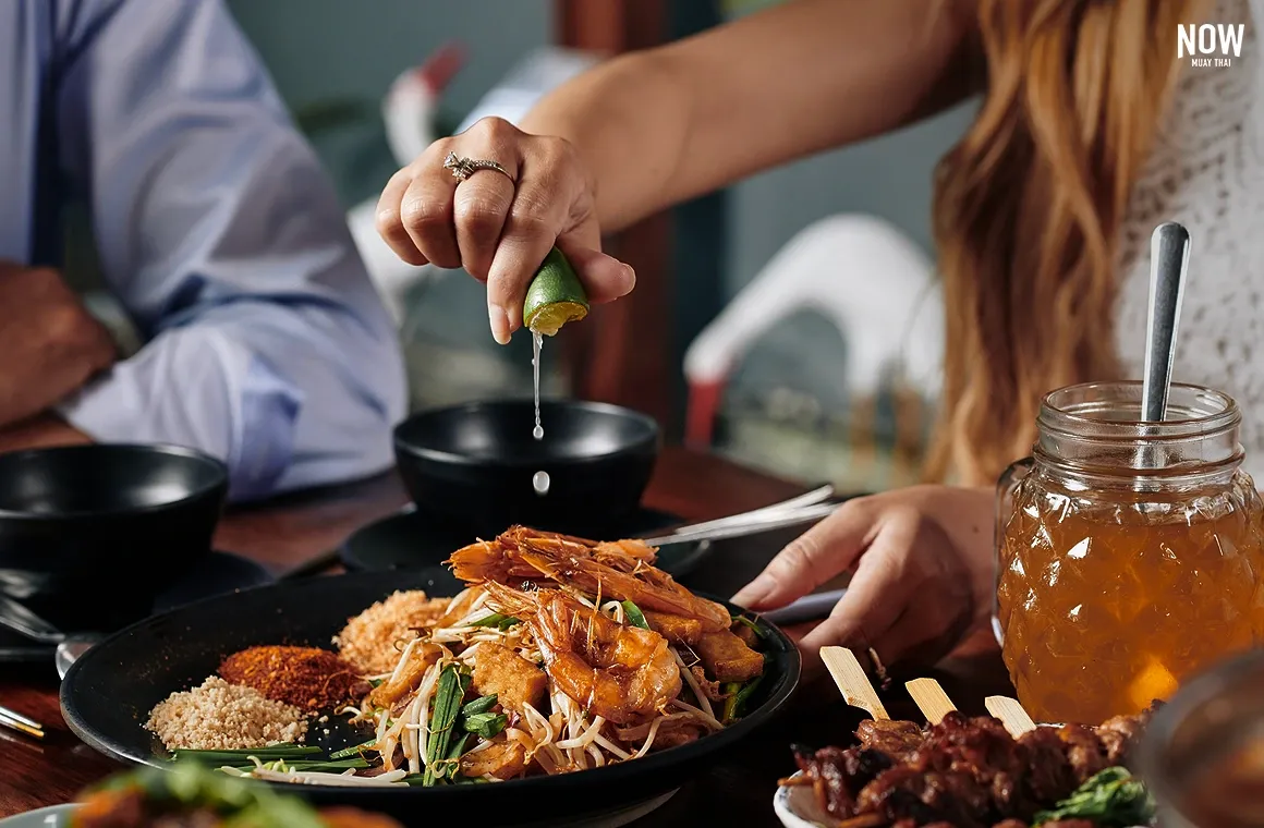 A woman squeezing lime into a dish of Pad Thai, one of the most popular dishes among foreigners. In addition to Pad Thai, Thai cuisine is renowned for its nutritious and low-calorie meals. Whether enjoying fine dining or street food, a visit to Thailand wouldn't be complete without sampling its famous culinary offerings.