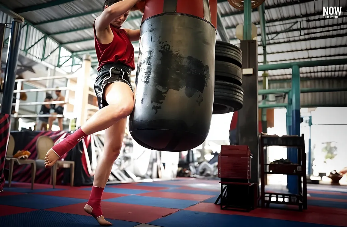 A woman jumping during a Muay Thai training session with a black barrel to enhance intensity, enjoying fitness and practicing her knee attack skills at a Muay Thai gym in Thailand.