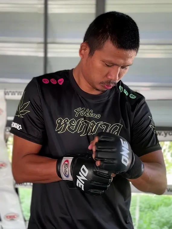 Superlek is putting on gloves before training with his trainer.