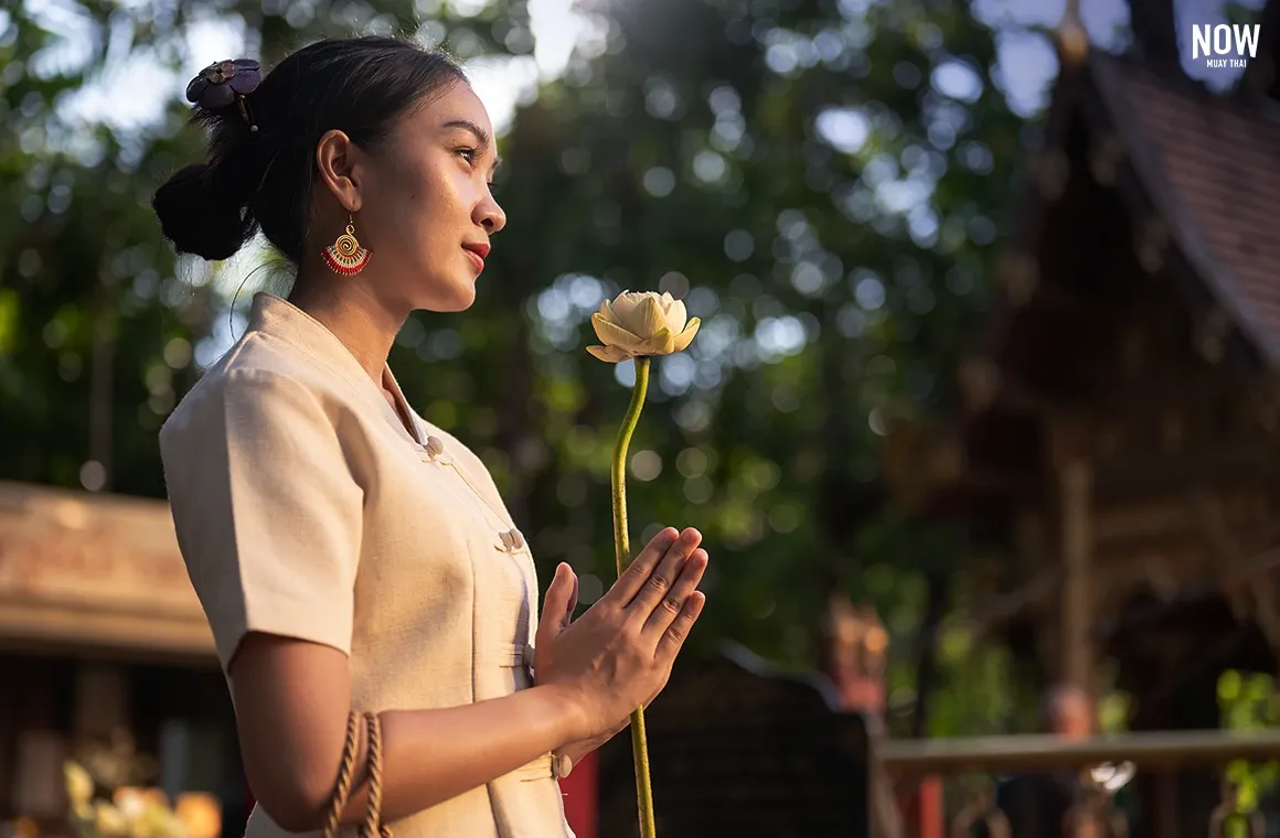 A beautiful Asian woman in traditional Thai Lanna dress makes a wish at a temple, reflecting Thai culture. The act of making merit and praying helps cultivate a calm mind, focus, and reduces stress.