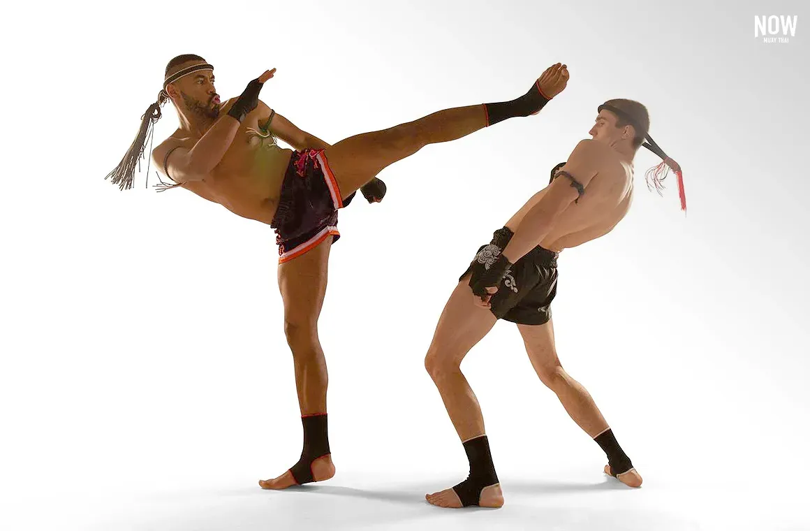 Two fighters demonstrate the Muay Thai technique of leaning to avoid a high kick, shifting weight onto the rear leg while keeping the head clear of the strike and maintaining balance.