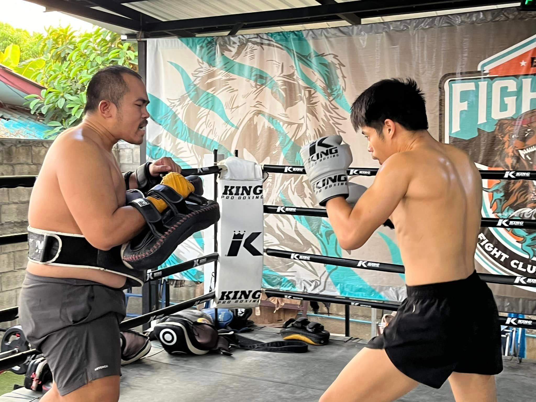 The trainer is coaching a student to strike the pad with punches.