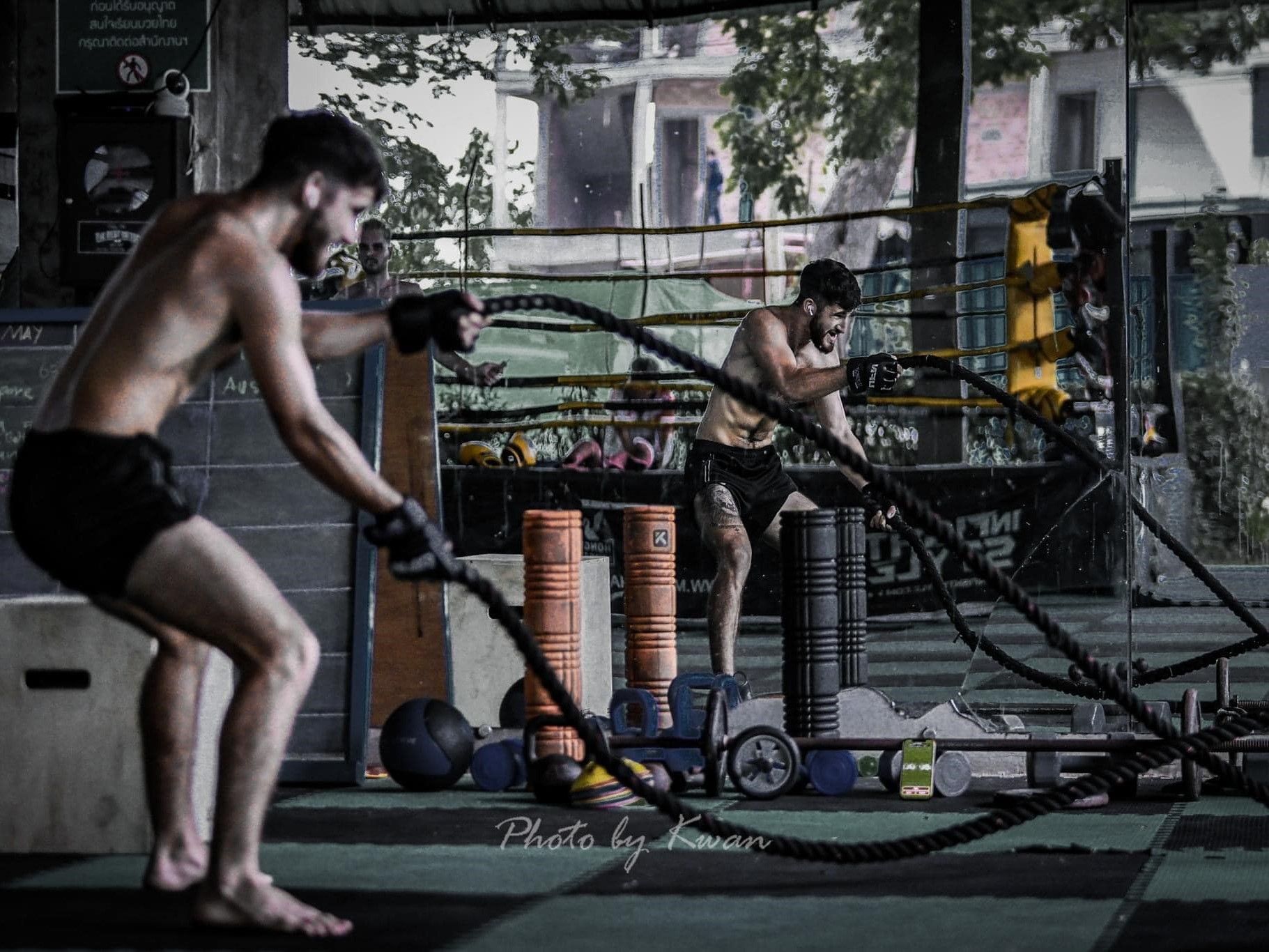 Man training with battle ropes in front of a mirror wall at the Hongthong Muay Thai Gym in Chiang Mai.