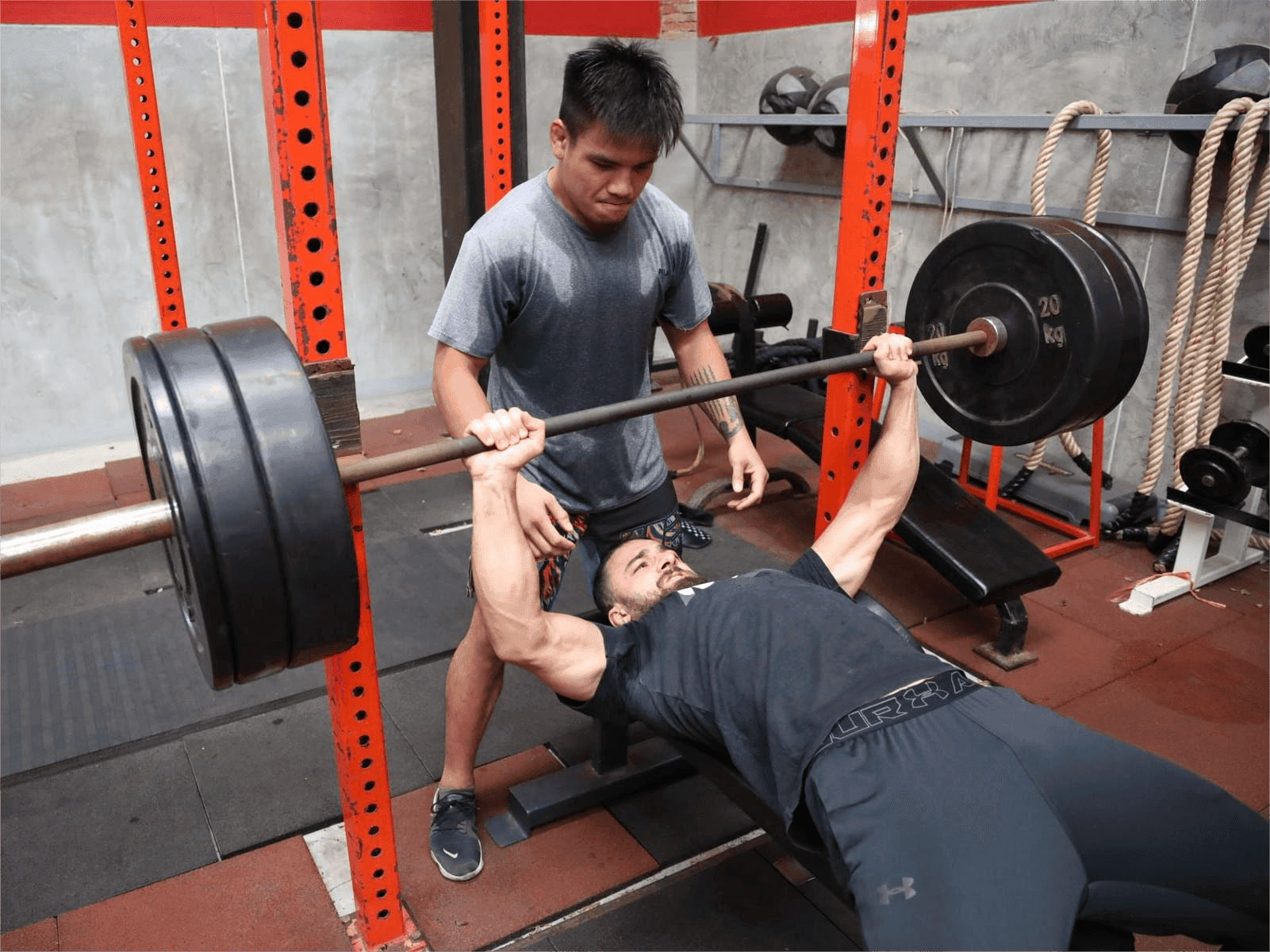 Athlete and his coach on the strength training session, lifting the iron barbell.