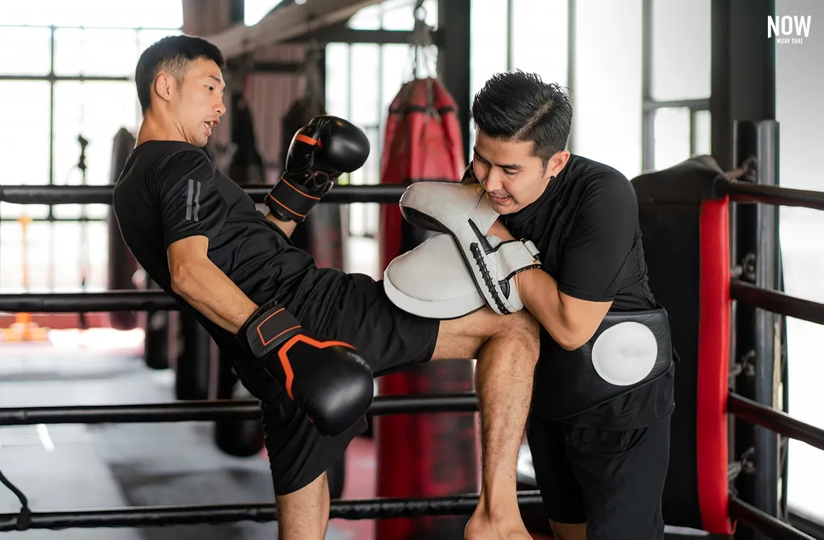Kickboxer improving skills by learning Muay Thai knee strike techniques with trainer, practicing close-range attack and defense in the ring.